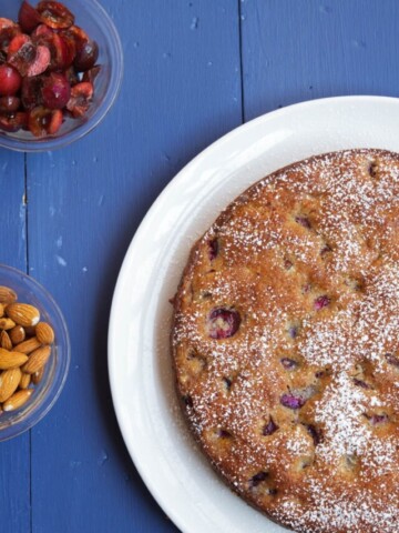 overhead partial view of cherry almond cake with bowls of cherries and almonds