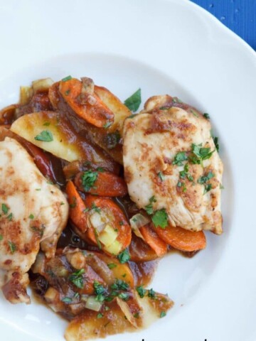 chicken thighs with carrots and apples in a Jack Daniels apple butter sauce sprinkled with parsley on a white plate