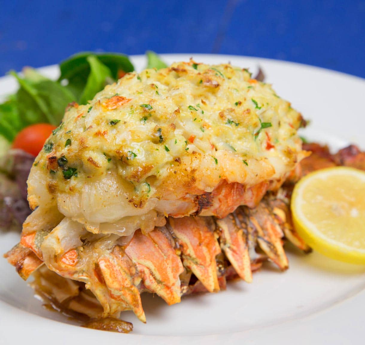 Stuffed lobster tail with crab imperial served on a white plate.