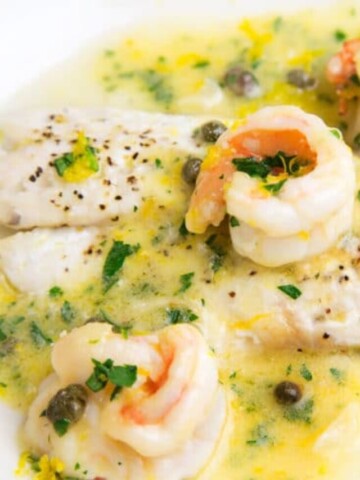 black seas bass topped with shrimp in a lemon caper sauce on a white plate