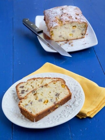 2 slices of peach pecan pound cake on a white plate with a yellow napkin under it and the rest of the cake on white platter