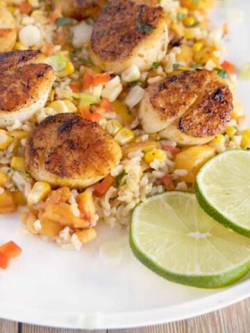 pan-seared scallops on a bed of rice with peaches and corn on a white oval platter