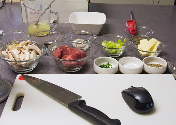 ingredients to make steak Diane, with a knife and wireless mouse on a white cutting board