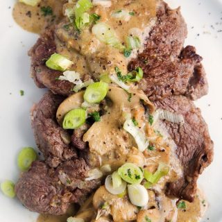 A white plate with filet slices topped with Steak Diane Sauce