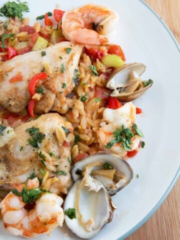 An overhead view of Chicken and Shrimp Orzo Paella on a green rimmed off white plate on a wooden cutting board