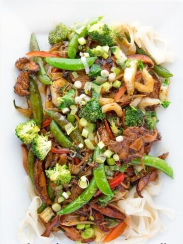 Stir Fried Pork with vegetables on a bed of Ho Fun Noodles on a white platter