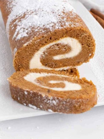 slice of pumpkin roll in front of the roll on a white platter