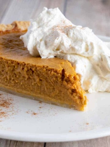 slice of creamy pumpkin pie with whipped cream on a white plate