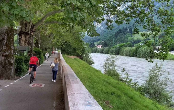 people walking and biking on the path along the Adige River in Trento