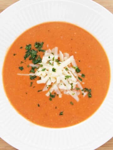 Tomato bisque in a white bowl with shredded cheddar cheese and parsley.