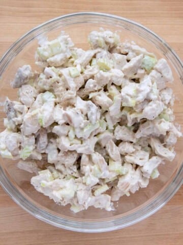 overhead view of chicken salad in a glass bowl on a wooden cutting board