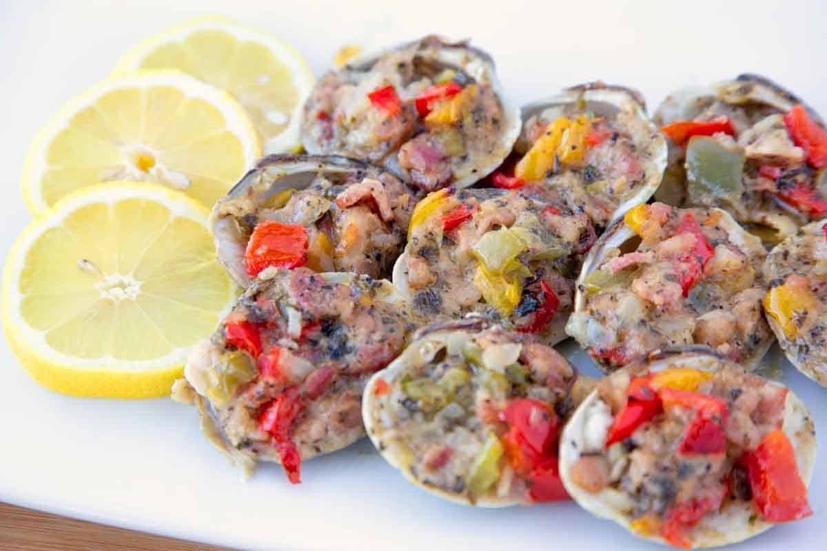 Close up of Clams Casino on a white platter with lemons.