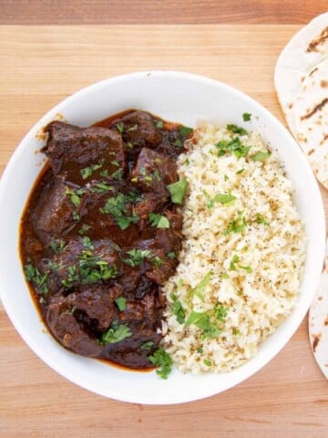 overhead view of a white bowl with beef chili colorado and rice with 4 small grilled flour tortillas on the side