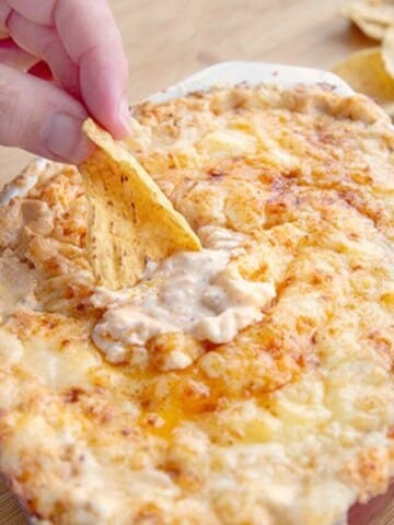 hand with a chip dipping into the cheddar lobster dip with chips around the dip