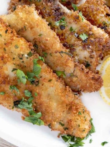 fried flounder filets on a white plate with lemon circles