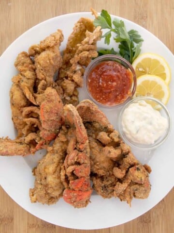 fried lobster tails with cocktail sauce and tarter sauce on a white plate