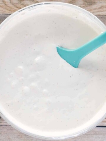 glass bowl of bleu cheese dressing with a blue rubber spatula in the bowl