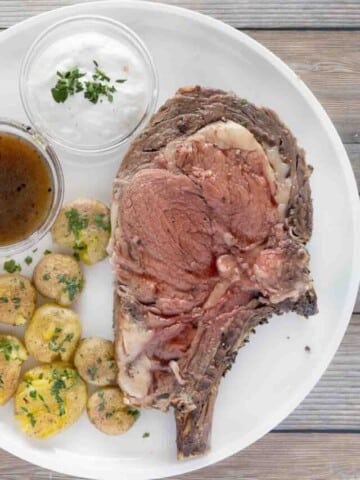 rare prime rib with smashed potatoes, au jus and horseradish sauce on a white plate