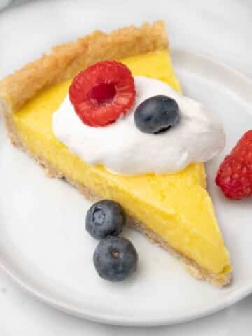 slice of lemon tart with whipped cream and berries on a white plate.