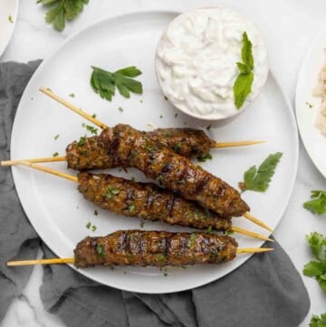 Kafta Kababs with a bowl of tzatziki sauce on a white plate.