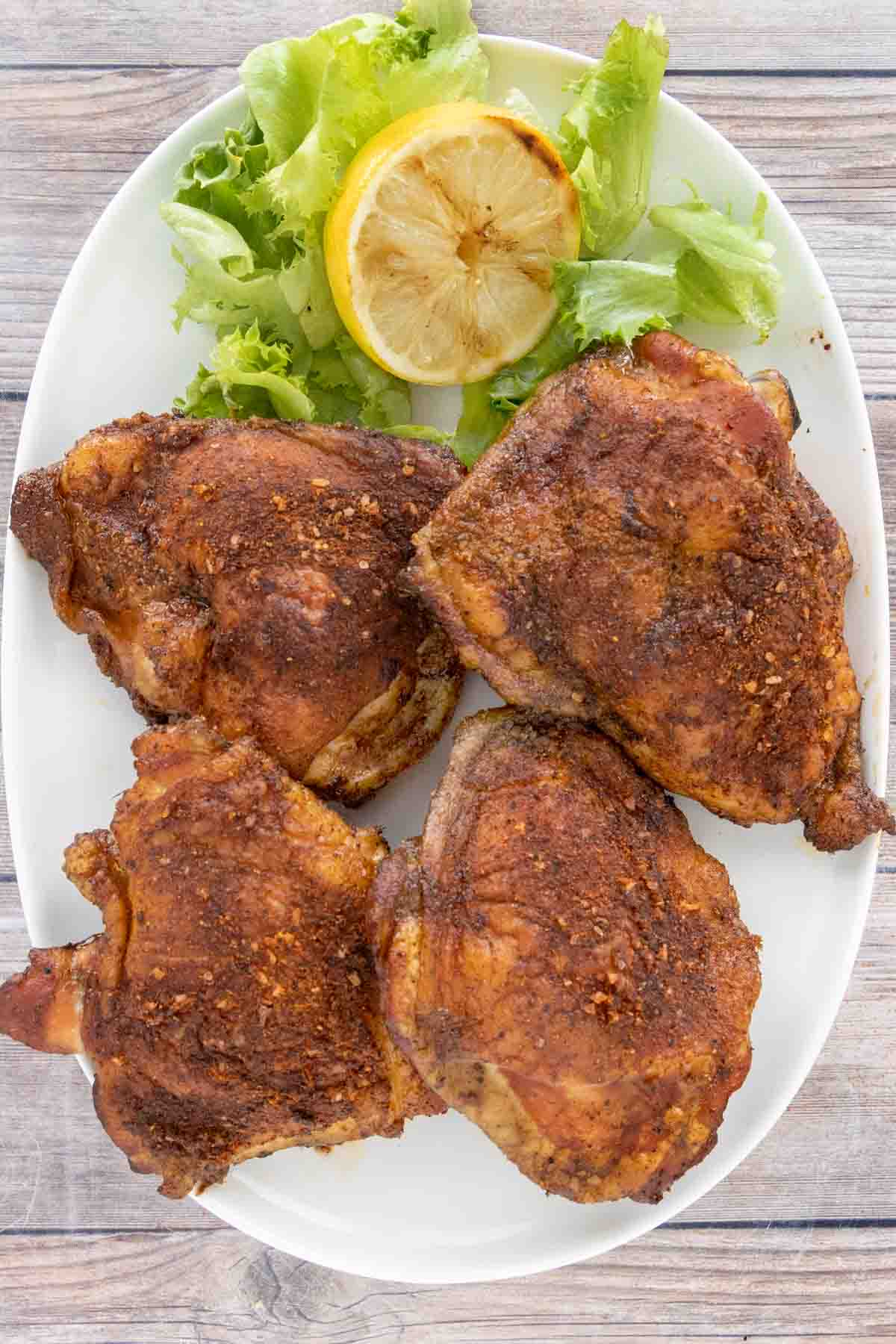 Smoked Chicken Thighs on a white platter with lettuce and smoked lemon half.