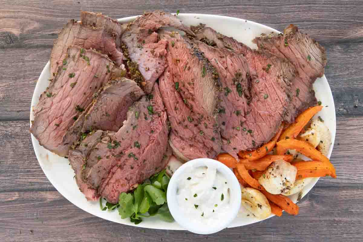 Sliced bottom round roast on a white platter with roasted vegetables.