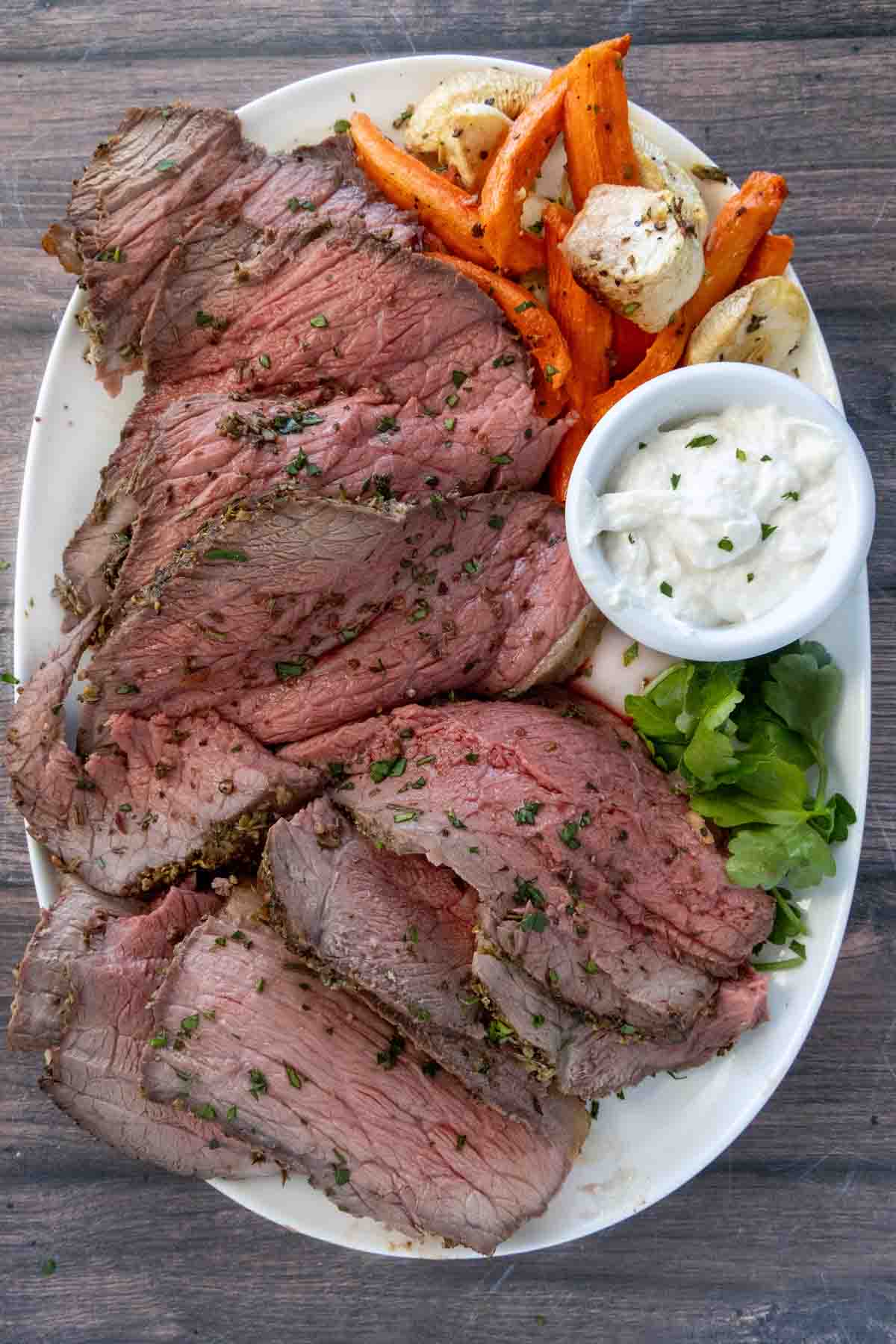 Sliced bottom round roast on a white platter with roasted vegetables.