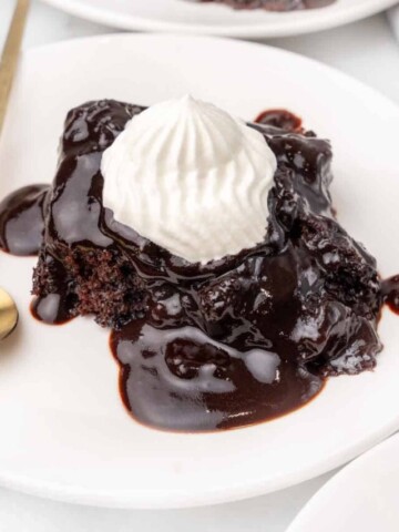 Chocolate pudding cake on a white plate with whipped cream.