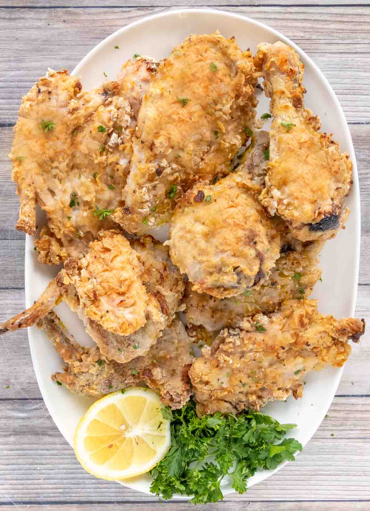 Oven fried chicken on a white platter with lemon and parsley.