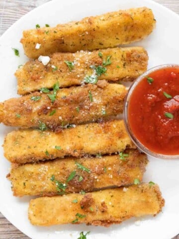 Mozzarella sticks with marinara sauce on a white plate.