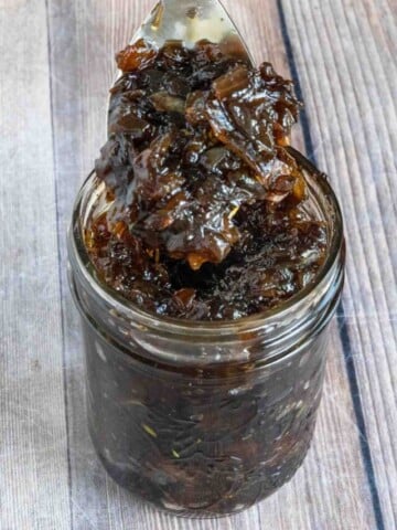 Caramelized onion jam in a glass jar with a spoon.