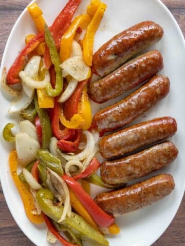 Smoked sausage, peppers, and onions on a white platter.