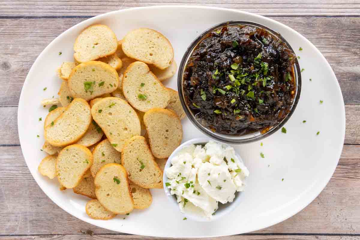 Caramelized onion jam on a white platter with toasts and goat cheese.