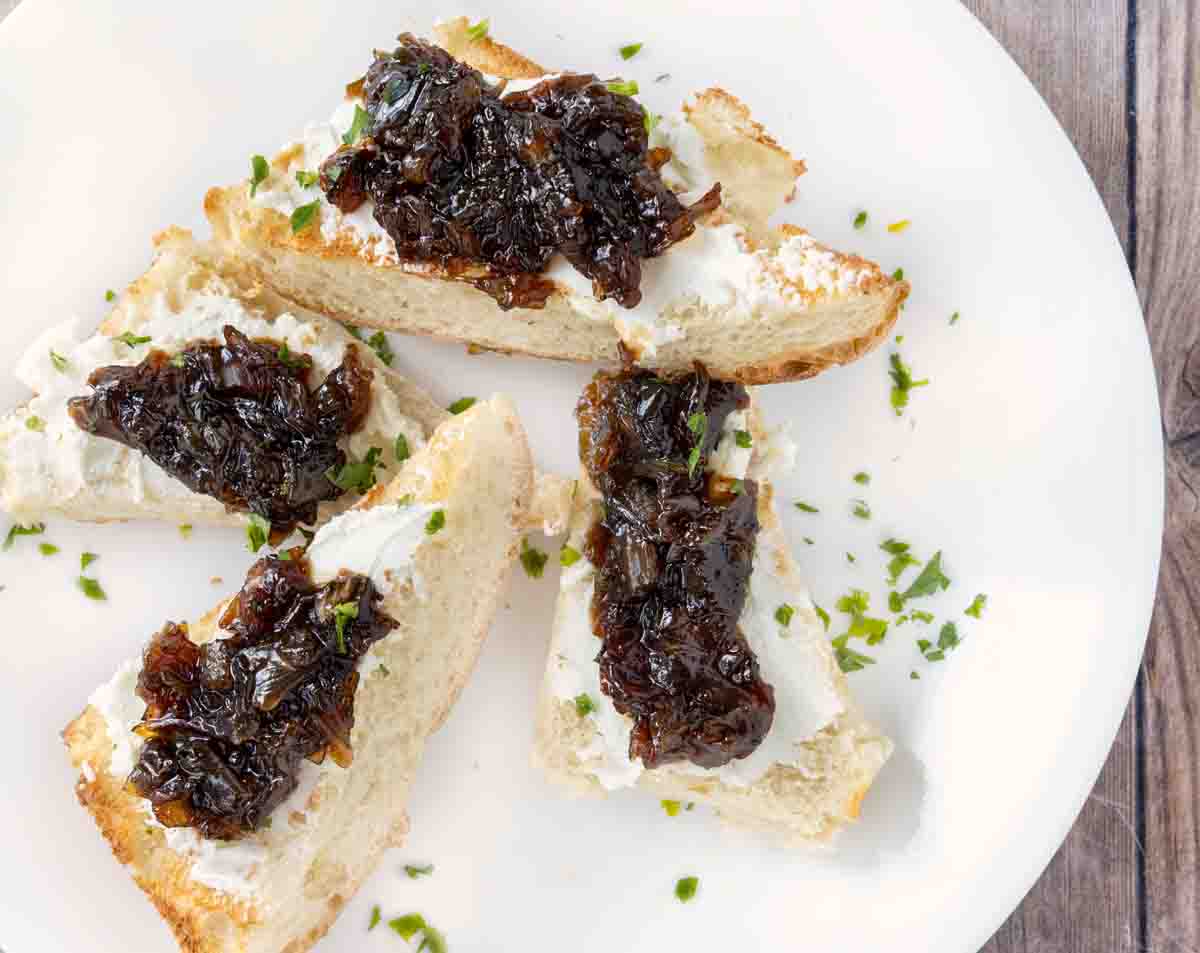 Toasts with goat cheese and caramelized onions on a white plate.