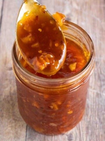 Honey sriracha sauce in a glass jar with a spoon coming out.