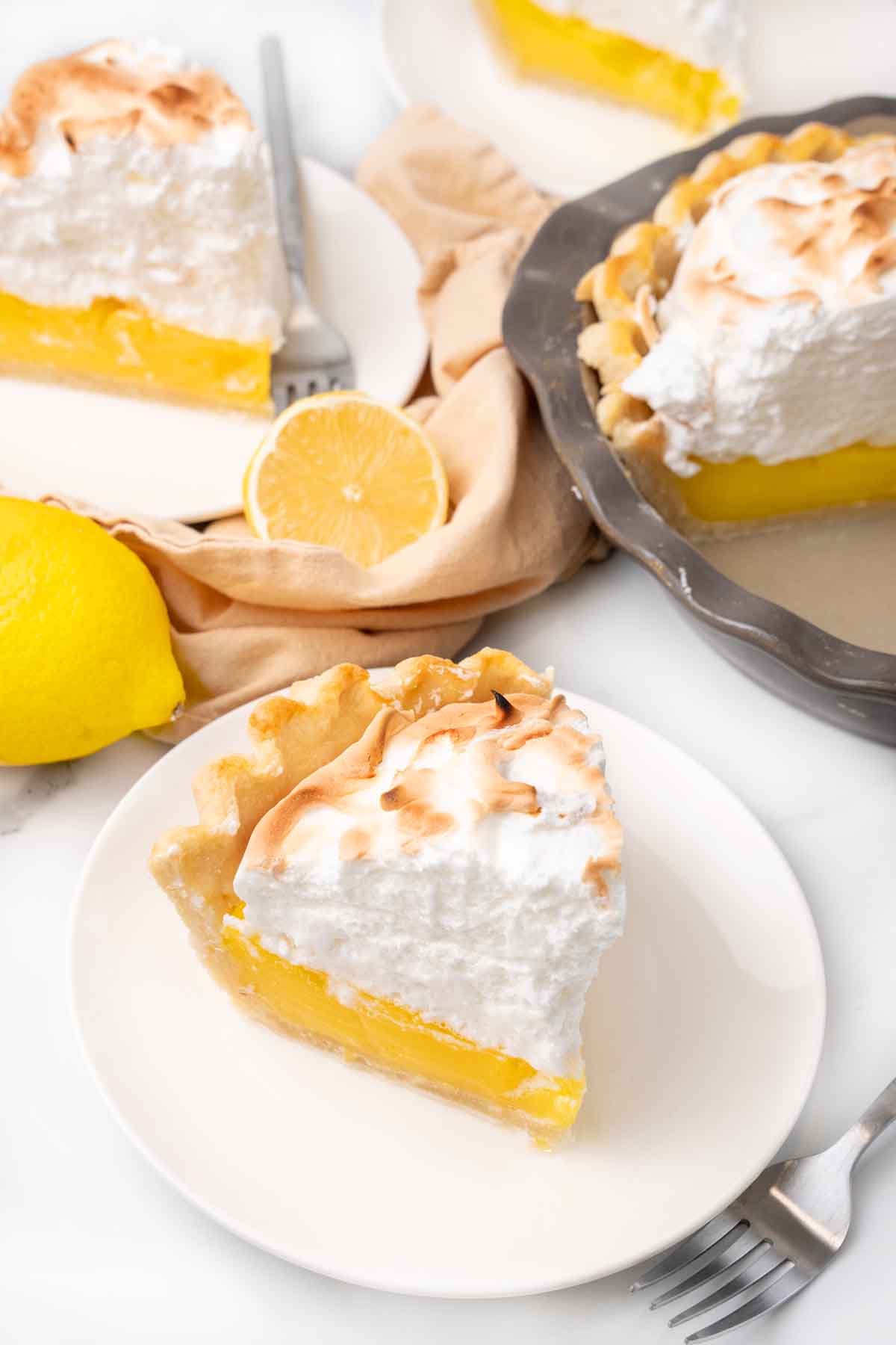 Slice of lemon meringue pie on a white plate with  more pie in the background