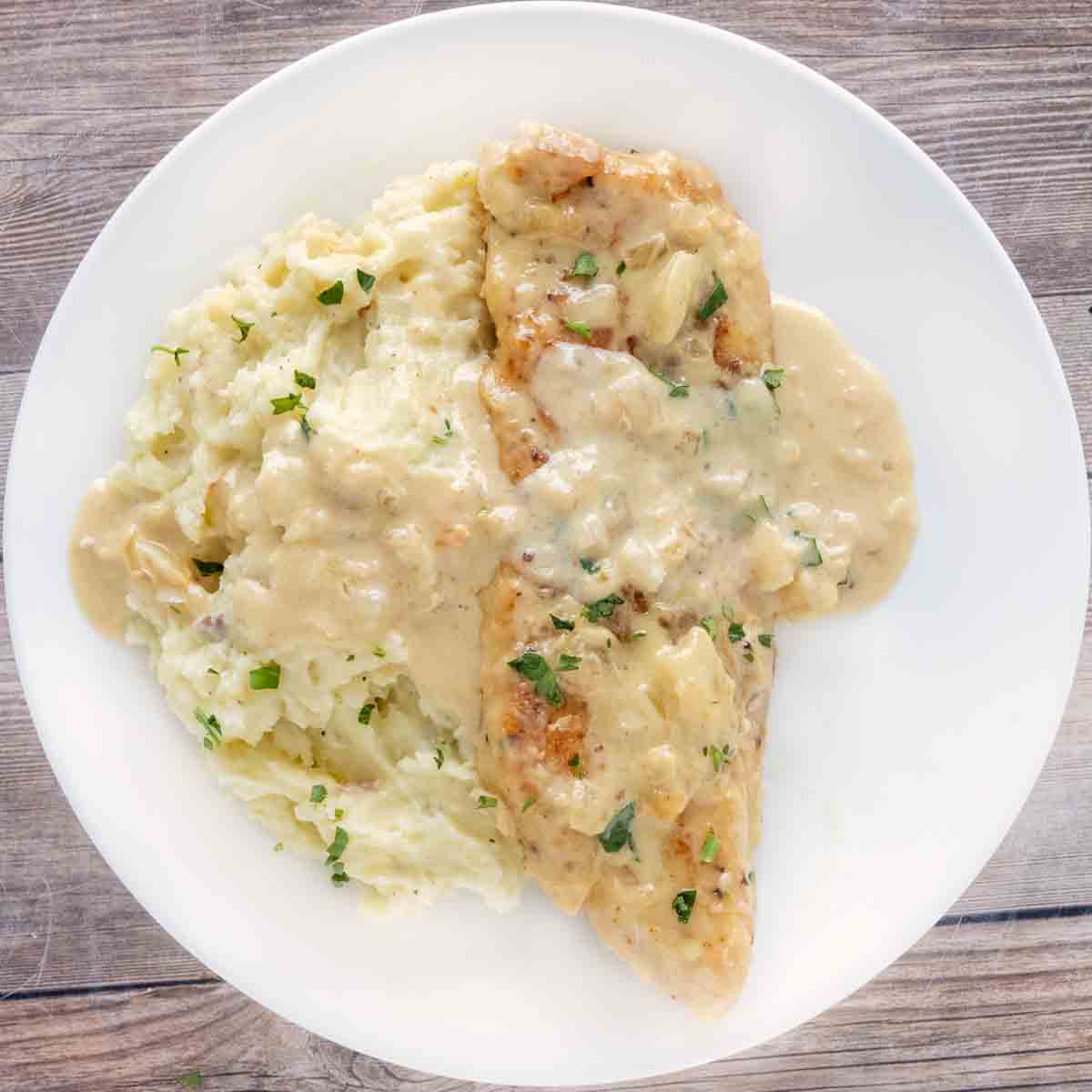 Creamy garlic chicken with mashed potatoes on a white plate.