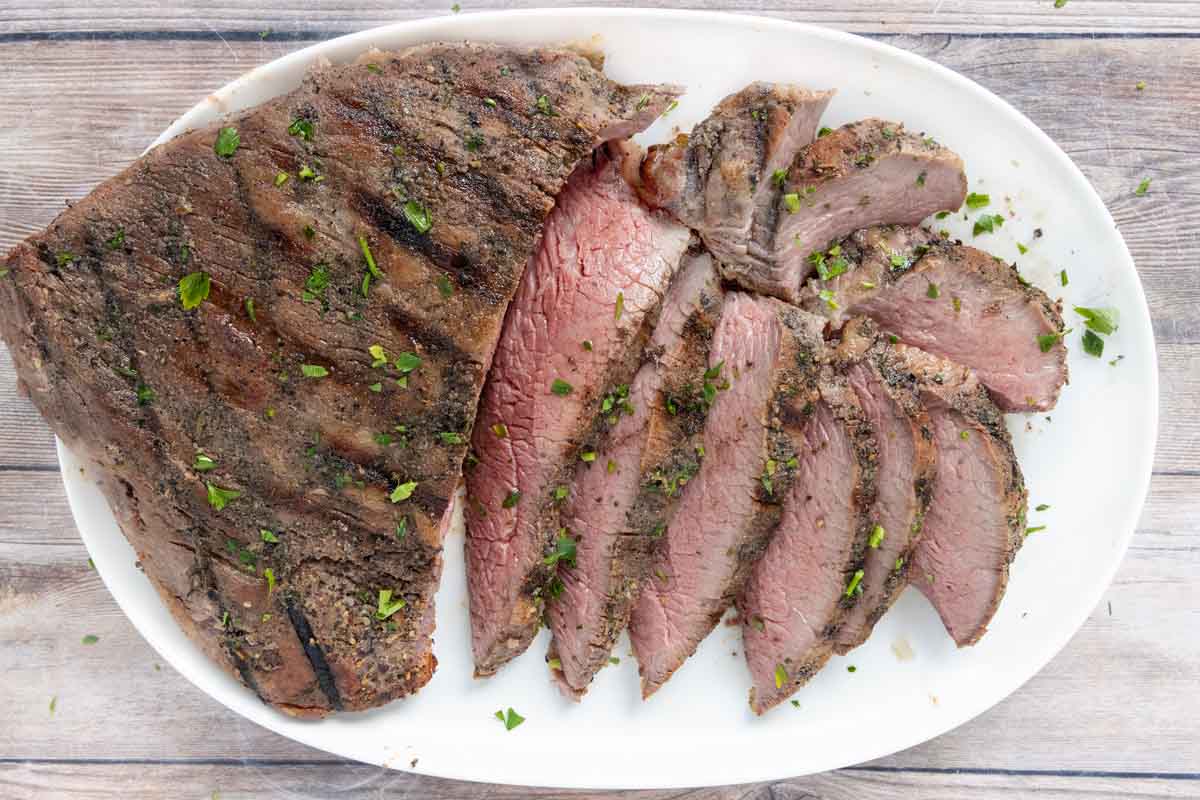 Sliced smoked tri-tip steak on a white platter.