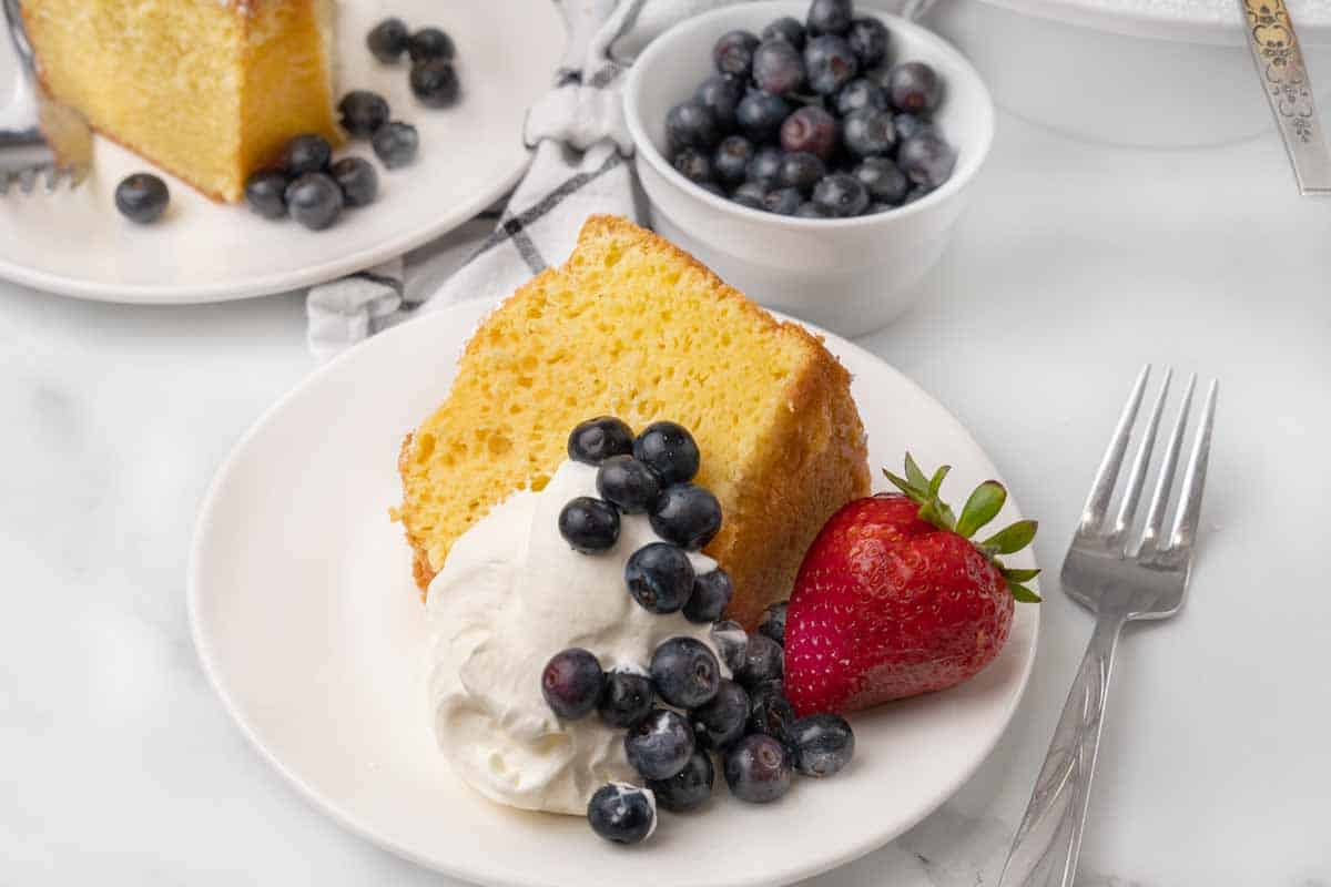 Slice of chiffon cake with whipped cream and berries on a white plate.