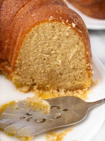 Sliced butter rum cake with cake spatula on white platter.