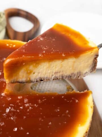 Slice of salted caramel cheesecake being taken out of the whole cake.