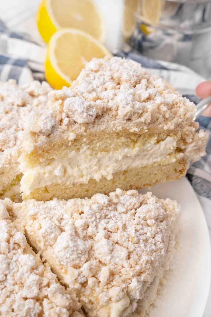 Slice of lemon cream cake being taken out of hte whole cake.