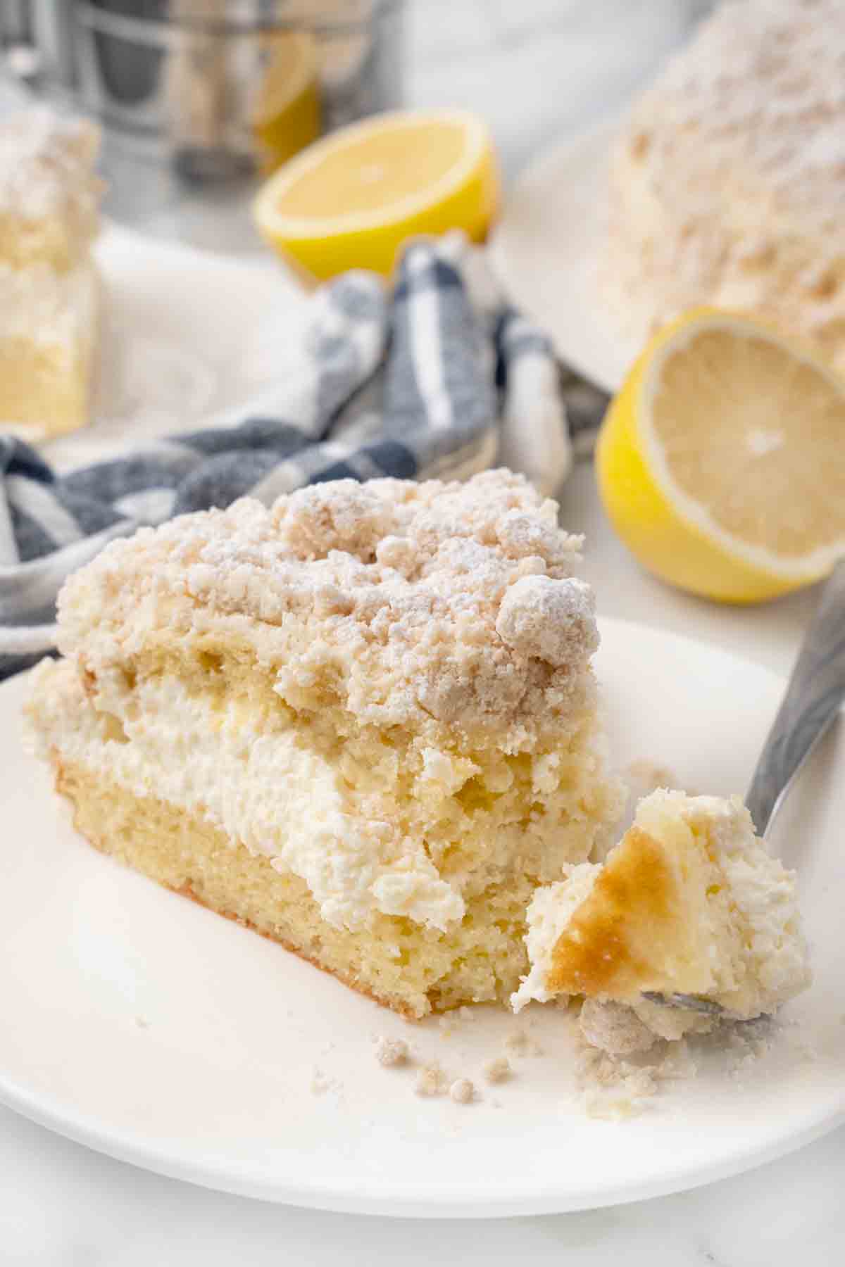 Slice of lemon cream cake on a white plate, with fork taking a piece out.