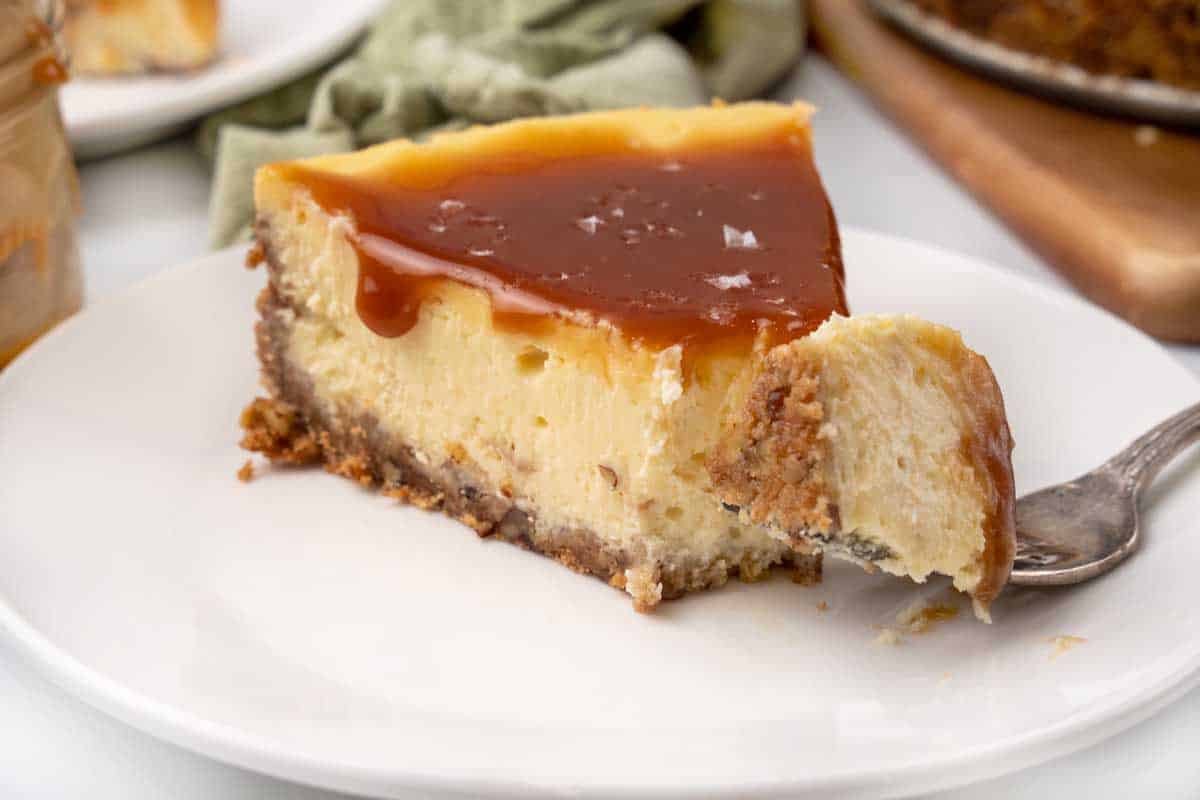 Slice of salted caramel cheesecake on a white plate with a fork taking a piece out.