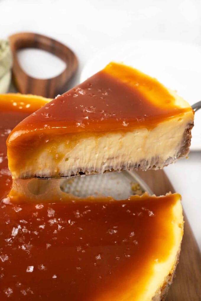 Slice of salted caramel cheesecake being taken out of the whole cake.