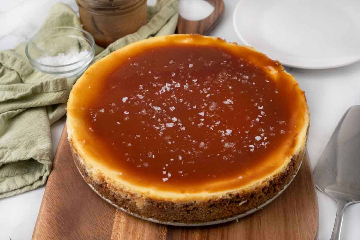 Whole salted caramel cheesecake on a wooden cutting board.