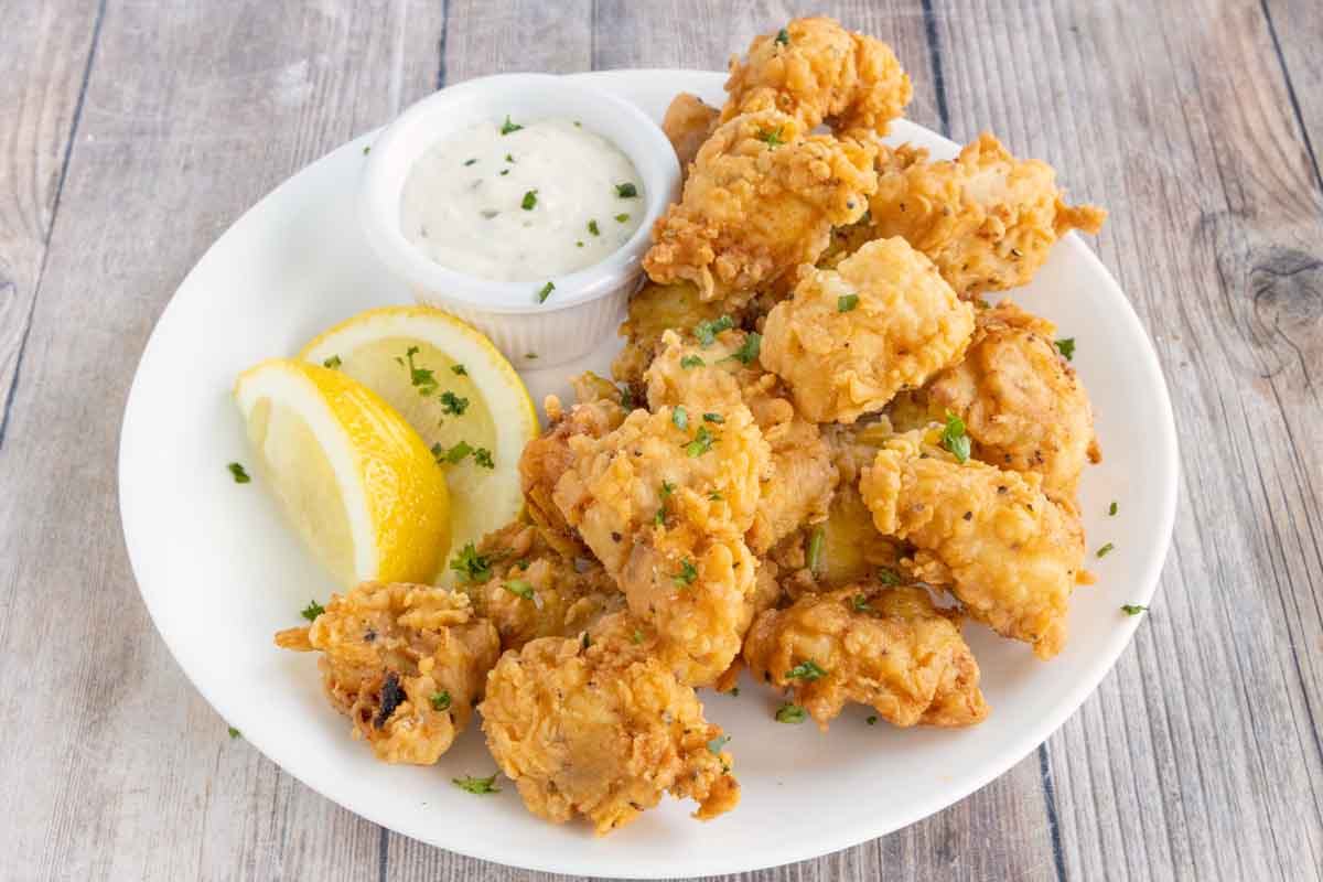 Catfish nuggets on a. white plate with tarter sauce and lemons.