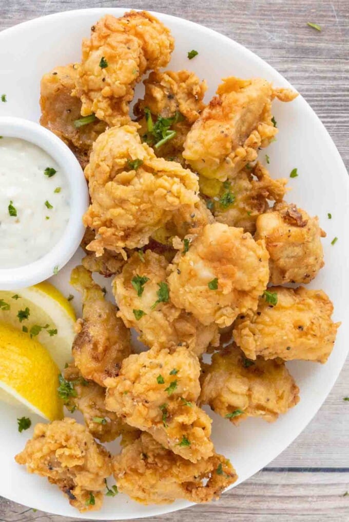 Catfish nuggets on a. white plate with tarter sauce and lemons.