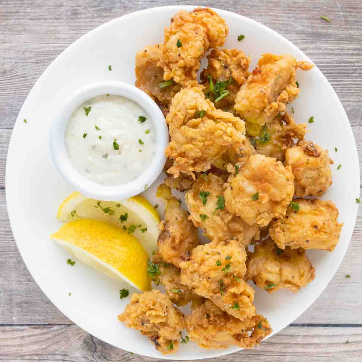 Catfish nuggets on a. white plate with tarter sauce and lemons.