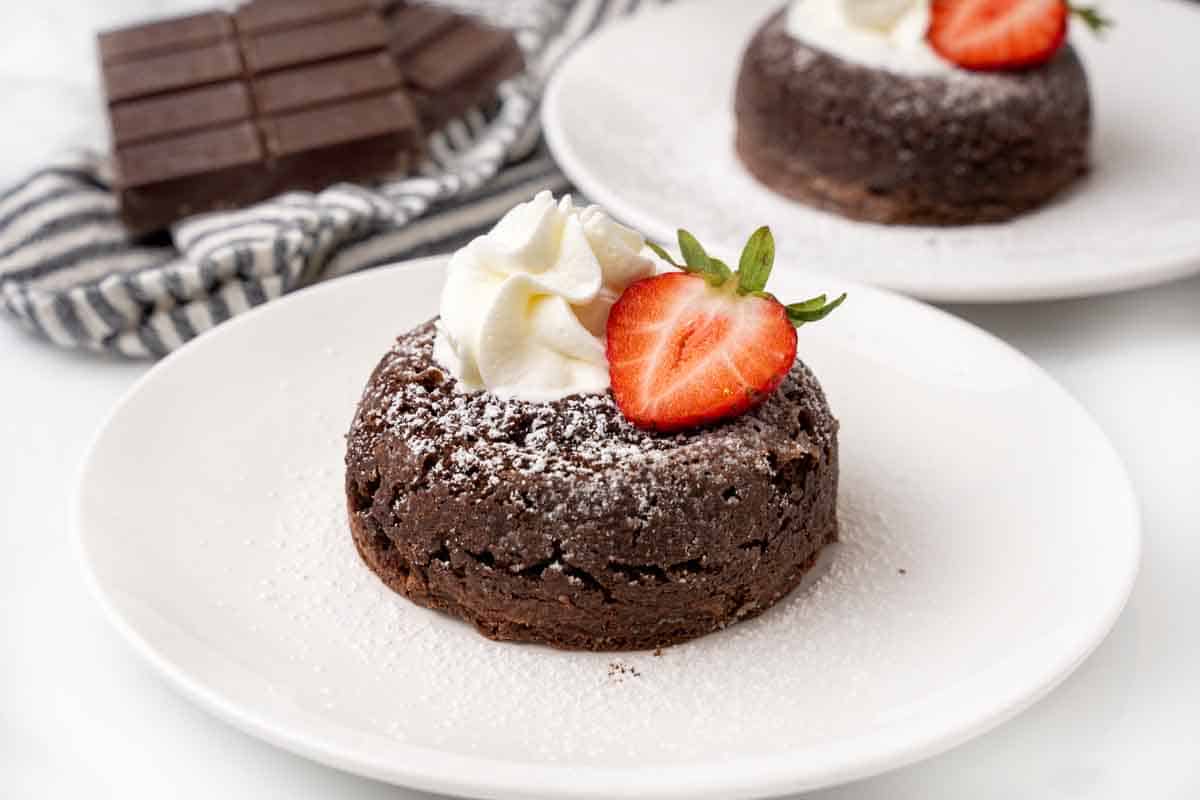 Lava cake topped with whipped cream and a strawberry slice on a white plate.